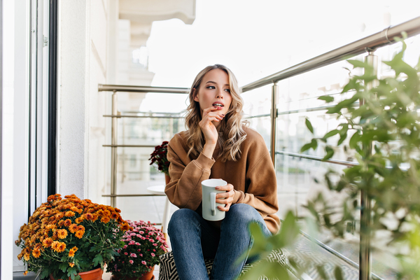 Frau mit Tasse auf bepflanztem Balkon